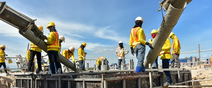 foto de uma série de trabalhadores da construção civil, devidamente equipados com os dispositios de segurança, em um canteiro de obras